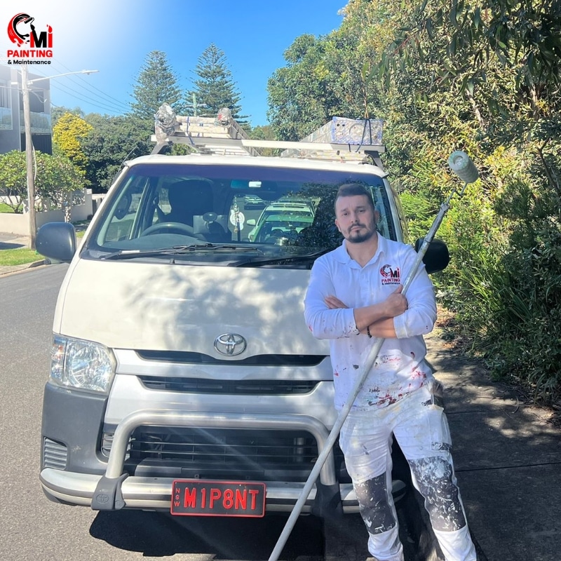 A commercial painter in Sydney standing next to a white van with a paint brush.