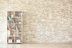 Modern bookshelf, styled for a homey feel, leans against a white brick wall. A perfect backdrop to showcase the subtle differences between whitewash vs limewash vs German Smear finishes.