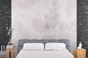 Bedroom featuring a grey headboard and white bedding, framed by black brick walls on either side and a central wall with a limewash finish. The image demonstrates the contrasting styles of whitewash vs limewash vs German smear.