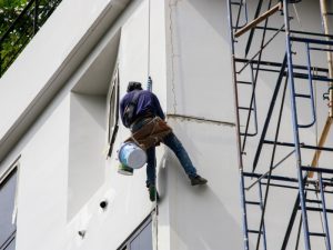 Worker performing rope access painting on a commercial building façade.