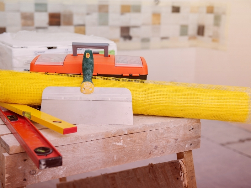 Plastering tools including a trowel, mesh, and level on a workbench. 