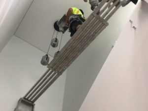 Worker on scaffolding performing drywall plastering in a high-ceilinged space, ensuring a smooth and durable wall finish.