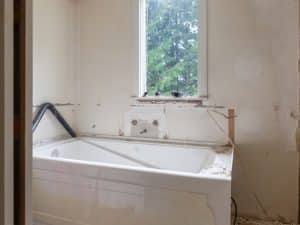 Bathroom in the demolition process with plumbing exposed, window view, and bathtub partially removed.