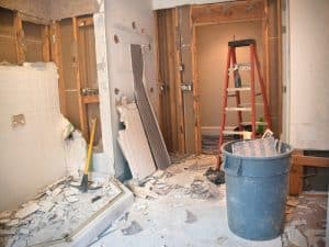 A bathroom demolition process mid-way, with debris, tiles, and broken walls showing, and tools scattered around.