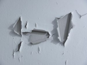 Close-up of paint cracking on an interior wall caused by temperature fluctuations and moisture.