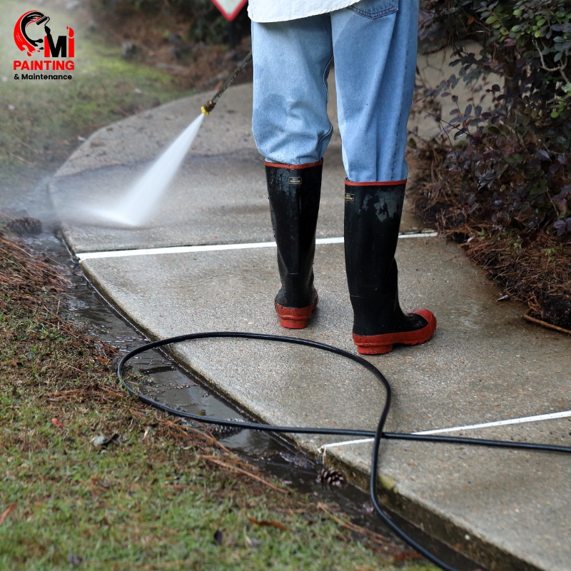 Worker performing concrete pressure cleaning on a sidewalk with a high-pressure hose, removing dirt and grime efficiently.