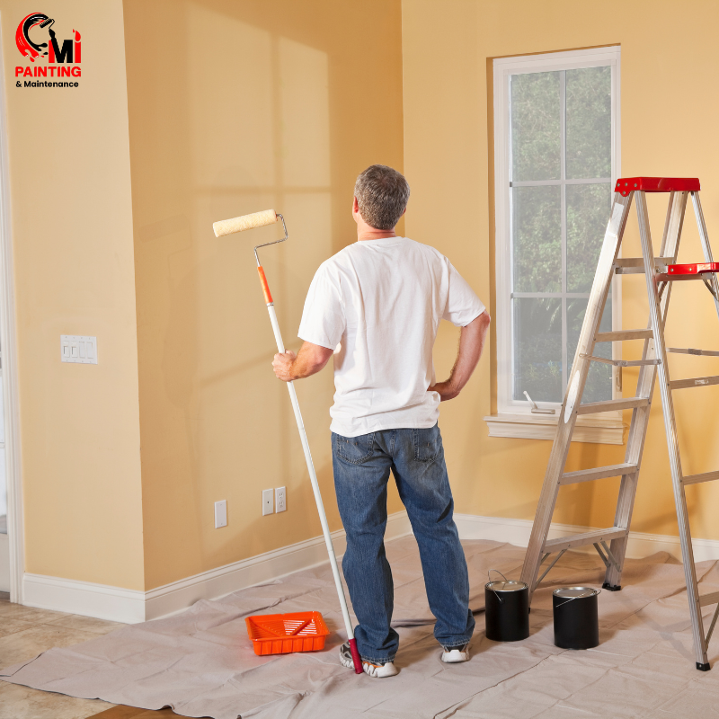 A professional painter working on residential painting in Sydney, painting a beige wall with tools and ladder nearby.