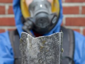 Worker in protective gear handling a pipe suspected of containing asbestos, emphasizing safety in bathroom asbestos removal.