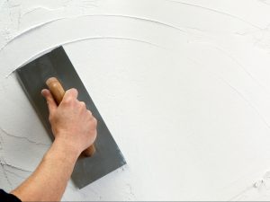 A hand holds a trowel smoothing wet plaster onto a wall, potentially reducing the risk of plaster cracking.