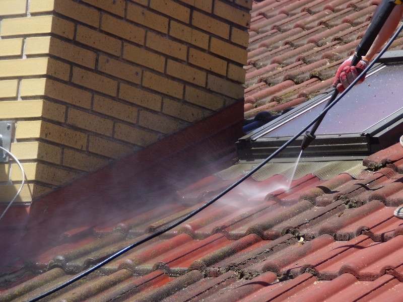 Roof pressure cleaning on tiled surface around skylight to remove moss and grime.