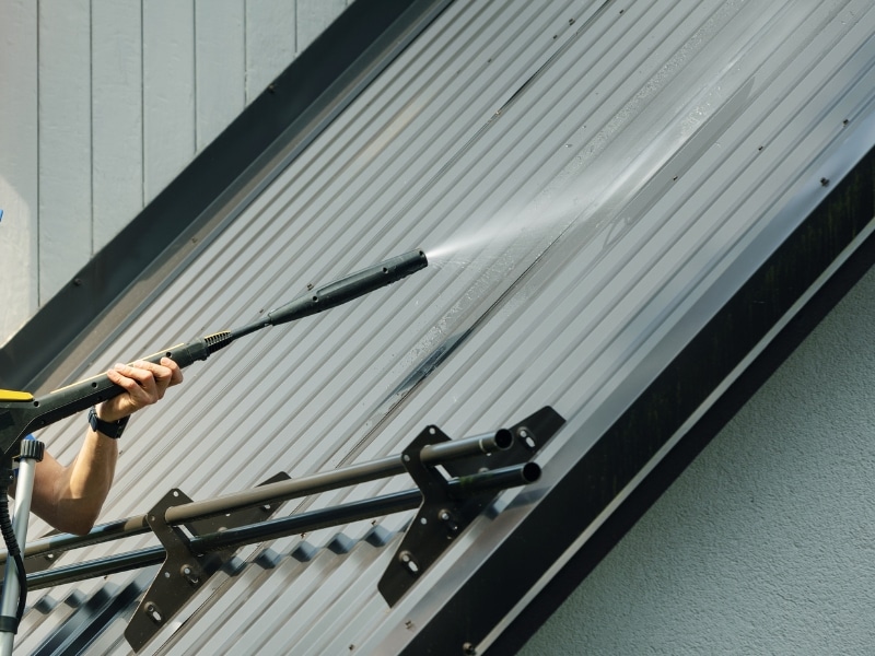 Roof pressure cleaning on modern metal roofing to remove grime and mildew.