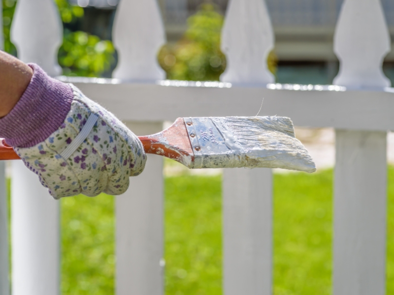 Gloved hand applying white fence painting colours on timber picket