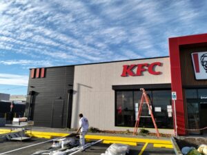Painter applying fresh exterior paint on a commercial building in Sydney with KFC signage under a bright blue sky